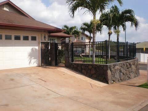 Aluminum fence on rock wall with palm trees, Oahu